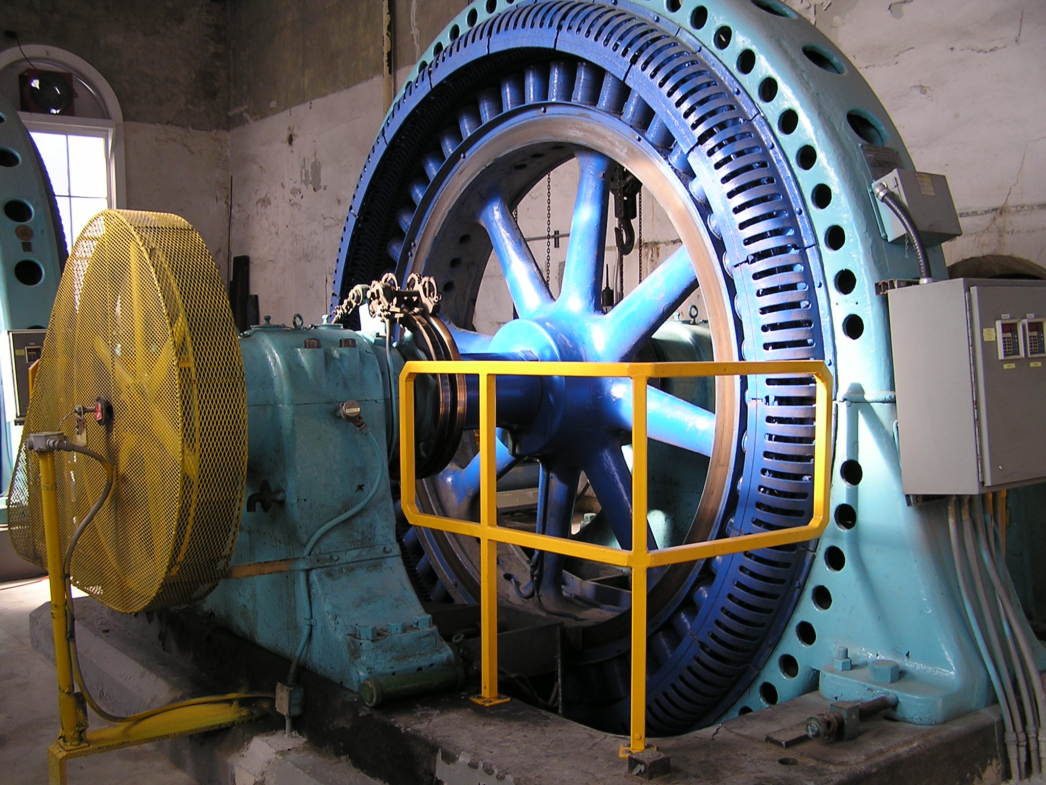 giant blue turbine wheel behind a yellow railing 